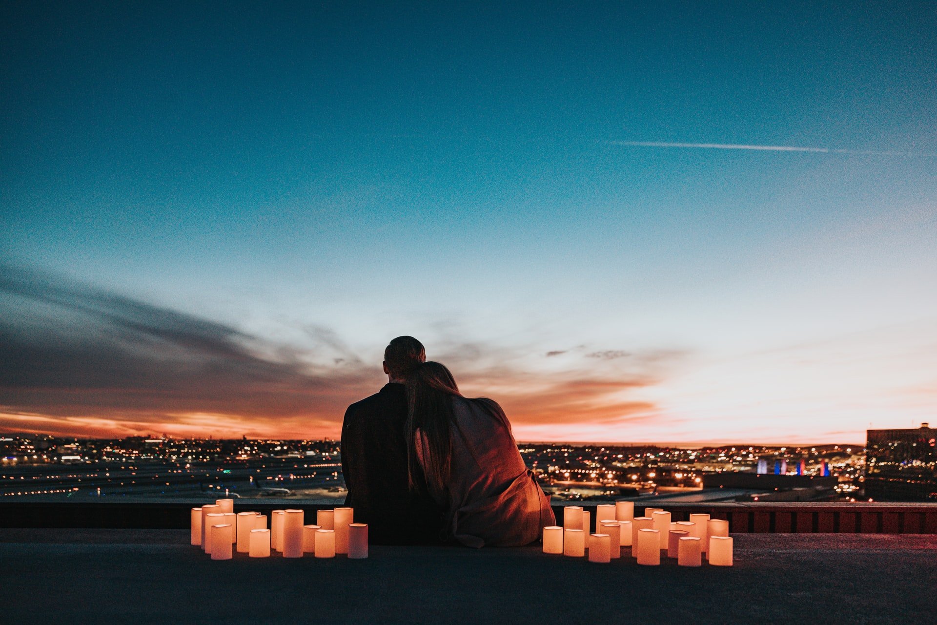 couple sits in the middle of candles overlooking city, leaning into each other, full of love, perfect moment captured