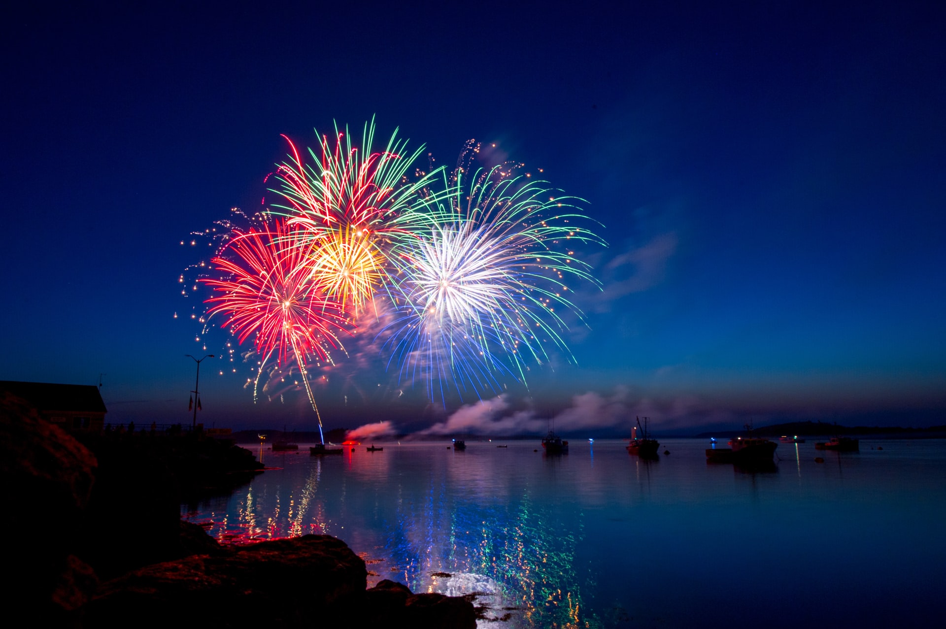 atmospheric photo of firework display over water, boats in the water