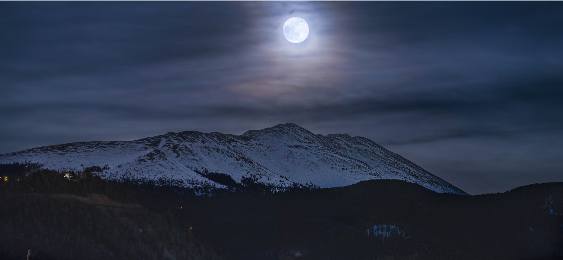 picture of full moon hanging over mountain range on a cloudy night