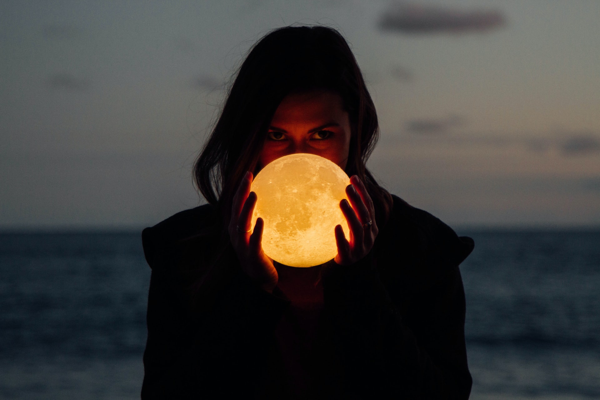 edited photo of a person facing the camera, holding the moon, glowing, between her hands