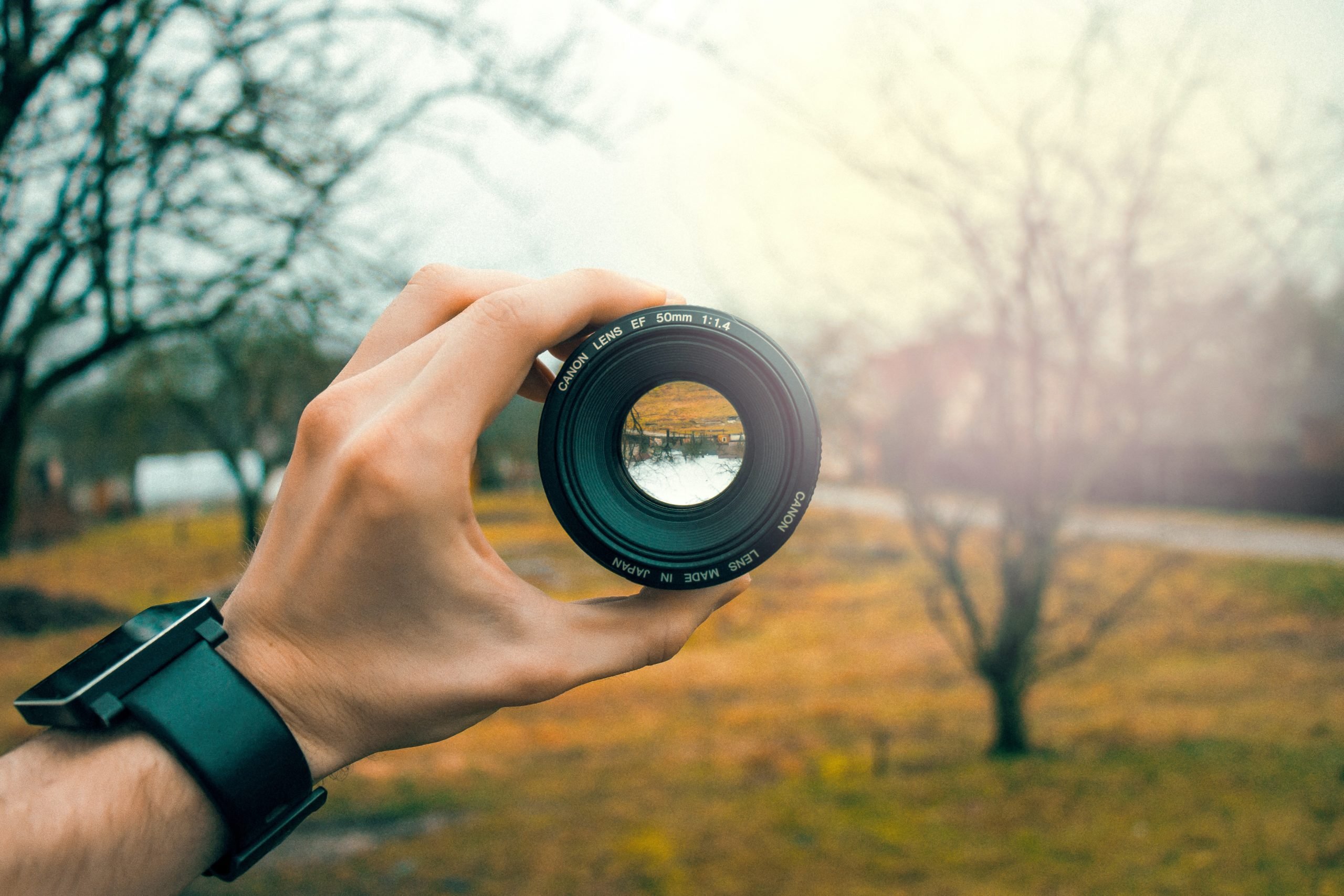person holding a camera lens in the centre of a rural grassy shot