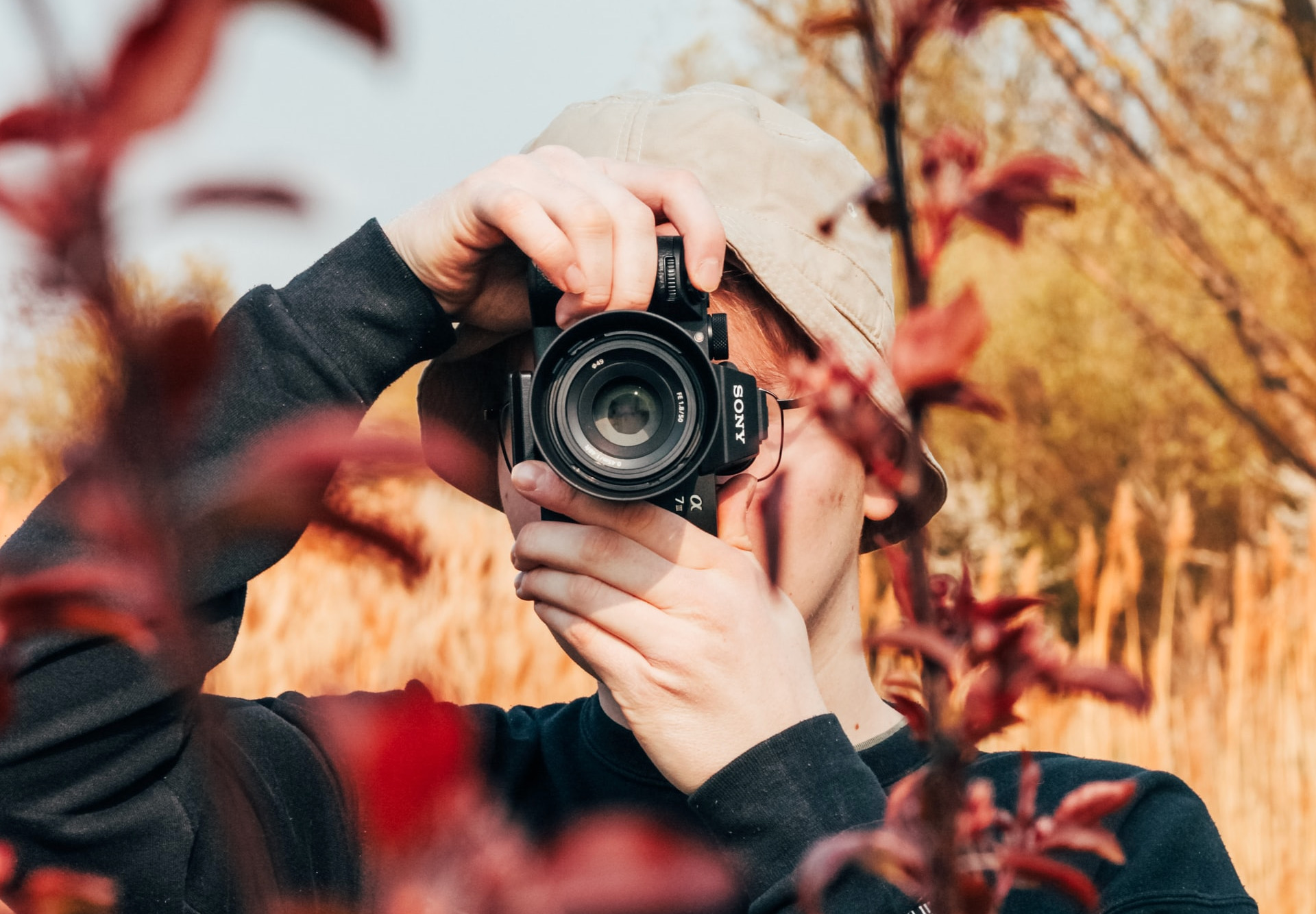 Photographer behind a Sony camera, in a field with autumn leaves in the shot