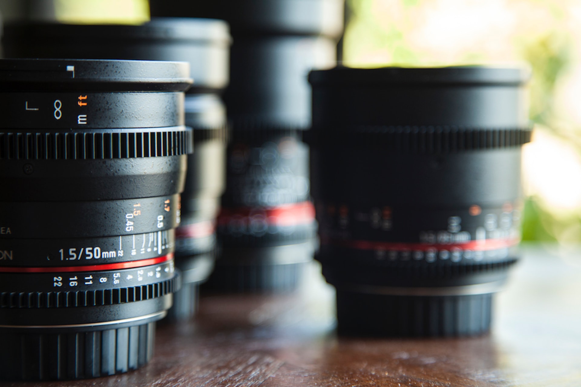 camera lenses on a wooden tabletop, plants in a blurred background