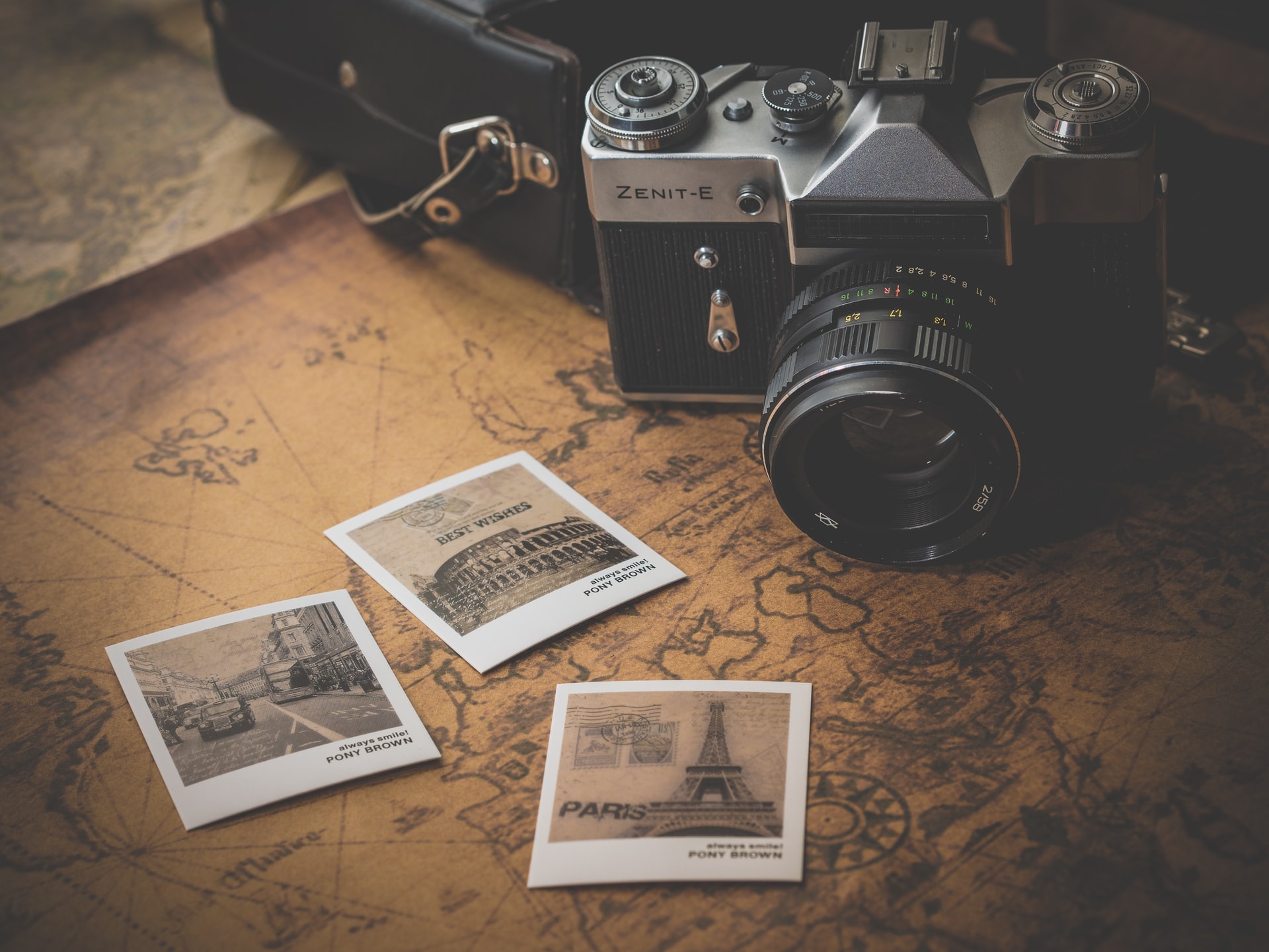 traditional DSLR film camera sits on a map next to 3 printed sepia photos